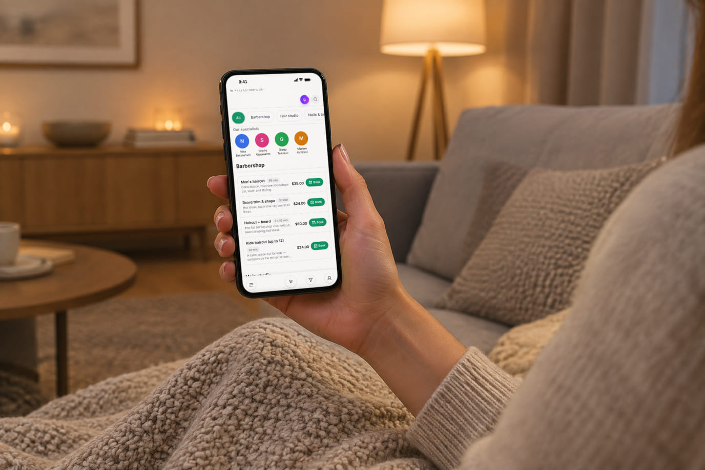 A client at home in the evening opens the salon booking page with specialists and services on her phone